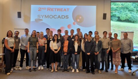 A group photo of the participants of the 2nd SyMoCADS Workshop in a conference room